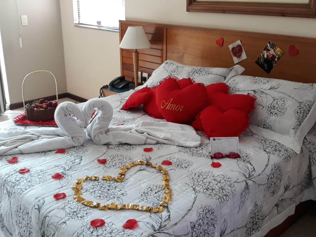 Cama decorada com corações, pétalas e cesta de morangos para o Pacote Noite Romântica